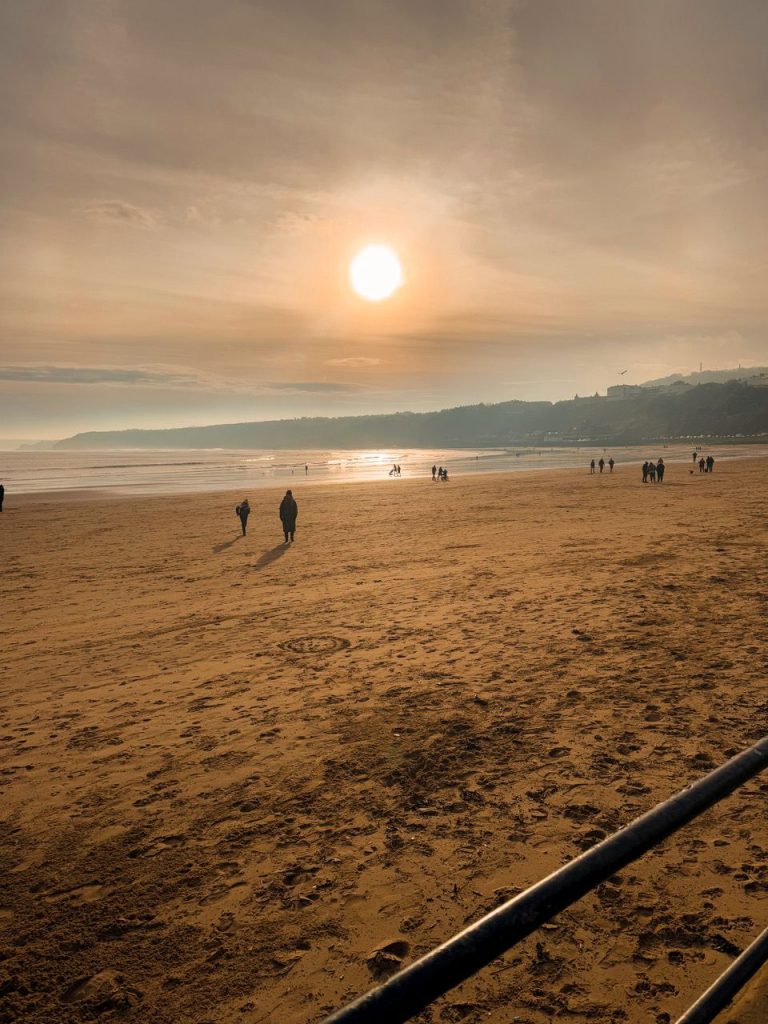Low winter sun over the wide wet sands of Filey beach, with walkers along the shore